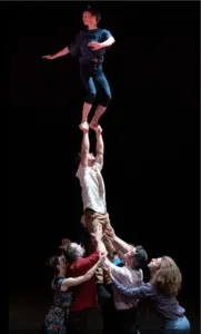 Een artiest balanceert op de handen van een acrobaat, gedragen door het hele collectief in een indrukwekkende menselijke piramide tijdens de voorstelling 'Wachten op de grote avond'.