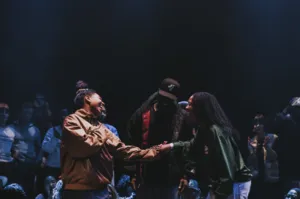 Foto van een dansbattle die dansers en publiek samenbrengt in een meeslepende sfeer. Twee deelnemers schudden elkaar de hand in het midden van de cirkel, onder het toeziend oog van de toeschouwers, wat de geest van delen, competitie en saamhorigheid illus