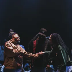 Foto van een dansbattle die dansers en publiek samenbrengt in een meeslepende sfeer. Twee deelnemers schudden elkaar de hand in het midden van de cirkel, onder het toeziend oog van de toeschouwers, wat de geest van delen, competitie en saamhorigheid illus