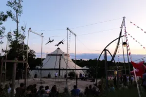 Foto van een grote trapezesessie georganiseerd bij CIAM in Aix-en-Provence. Een trapezeartiest hangt aan de trapeze boven een groot veiligheidsnet, onder een enorme overdekte constructie die natuurlijk licht doorlaat. Deelnemers