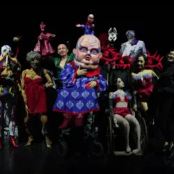 De artiesten van het gezelschap Succursale 101, omringd door grote poppen, hybride personages en fantastische kostuums in een donkere en dromerige sfeer.