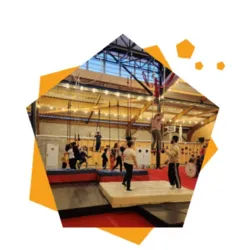 The hall of the La Carrière Circus Arts School in Saint-Barthélémy-d'Anjou during a circus workshop, with children practicing aerial disciplines, acrobatics and balance exercises on different apparatus.