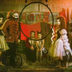 A scene of circus artists in costumes in front of a big top with an aerial hoop suspended in the foreground, illustrating the artistic universe and disciplines taught by Planet'Circus.