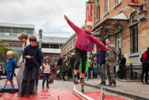 A young participant walks on a balance cable installed in front of the Tour & Taxis buildings in Brussels during an event organized by the Brussels Circus School, in front of an audience.