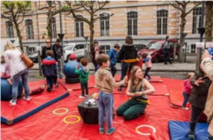 Multi-circus activity organised by the Brussels Circus School with several children discovering different disciplines of balance and juggling on safety mats in an outdoor space.
