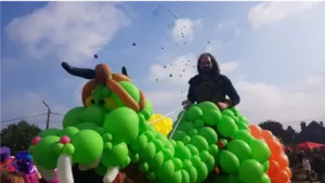 Trainer Maxime Duby creates an impressive balloon sculpture representing a green dragon during an outdoor event.