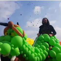 Trainer Maxime Duby creates an impressive balloon sculpture representing a green dragon during an outdoor event.