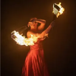 An artist in a red dress performs a fire fan display in the darkness. The flames create a wide, luminous arc around the dancer, illustrating the fire arts techniques taught during the Affectus Formation professional training program.