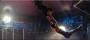Two flying trapeze artists perform a spectacular aerial figure in mid-air under a CIAM big top, illustrating the technical skill and artistic dimension of the Grand Flying Trapeze professional training.