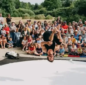 Contemporary circus performance in the open air during the Le Mans fait son Cirque festival: an acrobat performs a somersault in front of a large family audience gathered on the Promenade Newton in Le Mans.