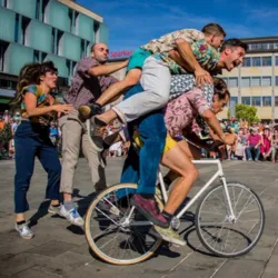 Nine artists from La Bande à Tyrex create an impressive human pyramid on an acrobatic bike in front of several hundred spectators during a circus performance in a public space.