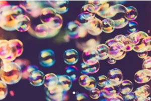Photograph illustrating numerous colorful soap bubbles floating in the air. The bubbles display iridescent, multicolored reflections against a dark background, illustrating the playful and scientific world of the soap bubble workshop.