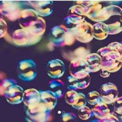 Photograph illustrating numerous colorful soap bubbles floating in the air. The bubbles display iridescent, multicolored reflections against a dark background, illustrating the playful and scientific world of the soap bubble workshop.