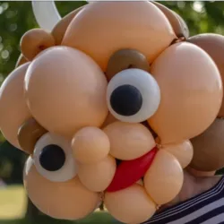 Close-up of a humorous face made entirely of flesh-colored balloons, with large expressive eyes and a red mouth, illustrating the expertise of Compagnie Bonnes Intentions in balloon sculpting.
