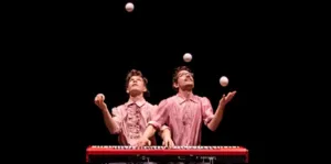 Twee artiesten van het Sombra Company jongleren met verschillende ballen rond een piano, een symbool van de ontmoeting tussen hedendaags jongleren en klassieke muziek.