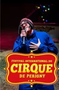 Een clown staat achter de microfoon onder de circustent met het rood-gele logo van het Internationale Circusfestival van Périgny.
