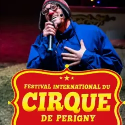 Een clown staat achter de microfoon onder de circustent met het rood-gele logo van het Internationale Circusfestival van Périgny.