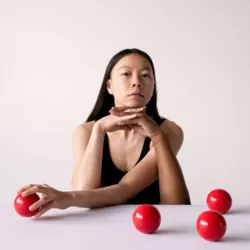 Een artiest van het Gandini Juggling gezelschap poseert voor een lichte achtergrond met vier rode jongleerballen, een afbeelding uit de show Heka – Het is allemaal maar een illusie, een mix van hedendaags jongleren en magie.