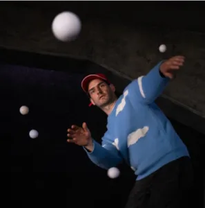 Een jongleur manipuleert verschillende stuiterende witte ballen in de podiumwagen van Post uit Hessdalen, een circusvoorstelling die in 2027 in Auray wordt gepresenteerd.