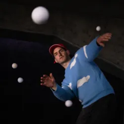 Een jongleur manipuleert verschillende stuiterende witte ballen in de podiumwagen van Post uit Hessdalen, een circusvoorstelling die in 2027 in Auray wordt gepresenteerd.