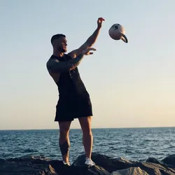 Pratique du Kettlebell Juggling par Cyril Monnaux en bord de mer, avec une kettlebell en rotation dans les airs pendant un enchaînement de jonglerie et de flow.